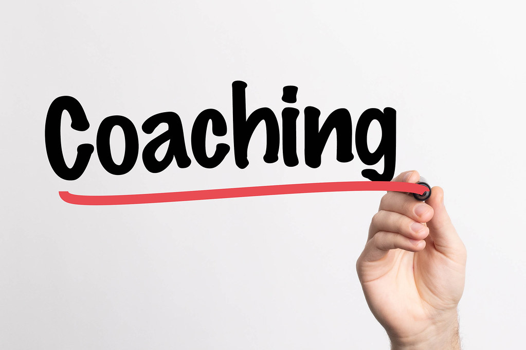 Auf dem Bild ist der Schriftzug Coaching zu sehen. Unter dem Schriftzug eine Hand, die den Schriftzug schreibt. Auf dem Bild ist der Schriftzug Coaching zu sehen. Unter dem Schriftzug eine Hand, die den Schriftzug schreibt.